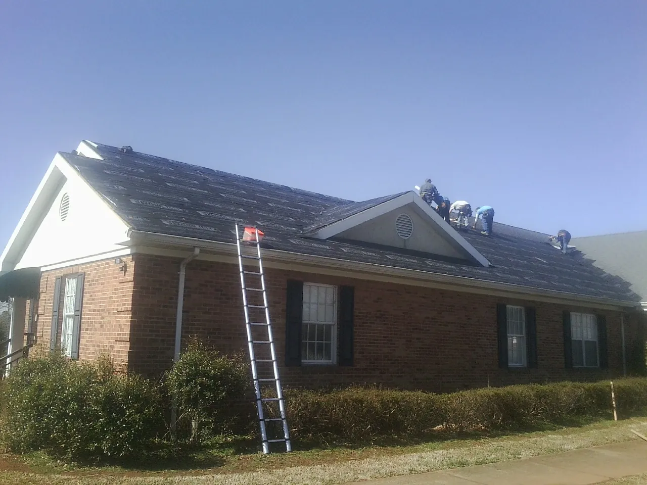 Crew tearing shingles off a brick ranch roof with a ladder set — Emergency Roof Repair work by our crew in South Berwick