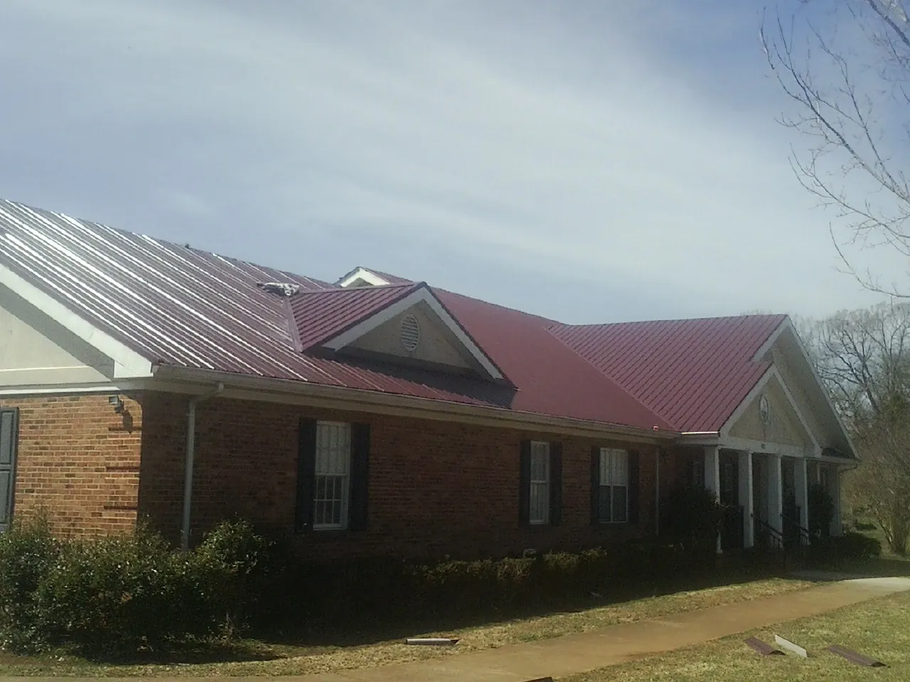 Red metal roof with gabled entries on a long brick building, from a Hail Damage Roof Repair job in South Berwick