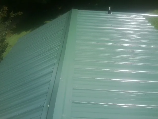 New green metal panels meeting at the ridge of a roof — Flat Roof Repair work by our crew in South Berwick