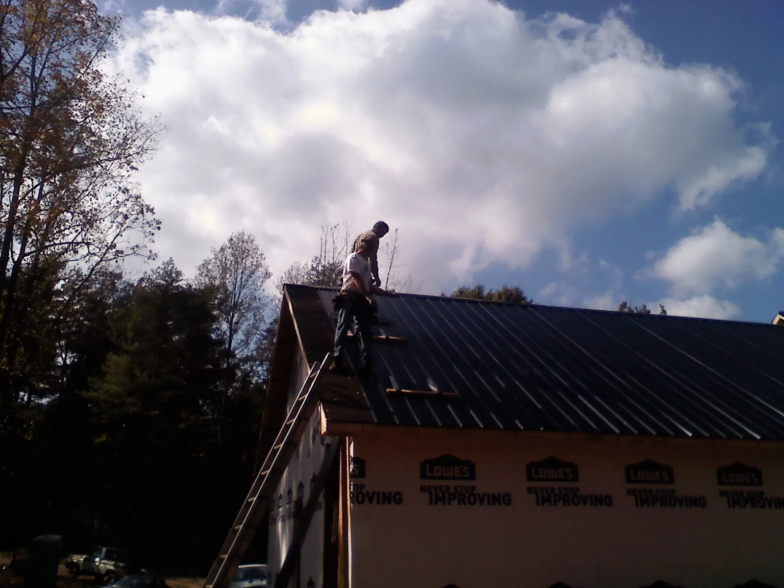 Roofer fastening dark metal panels high against a cloudy sky, from a Roof Inspection job in South Berwick