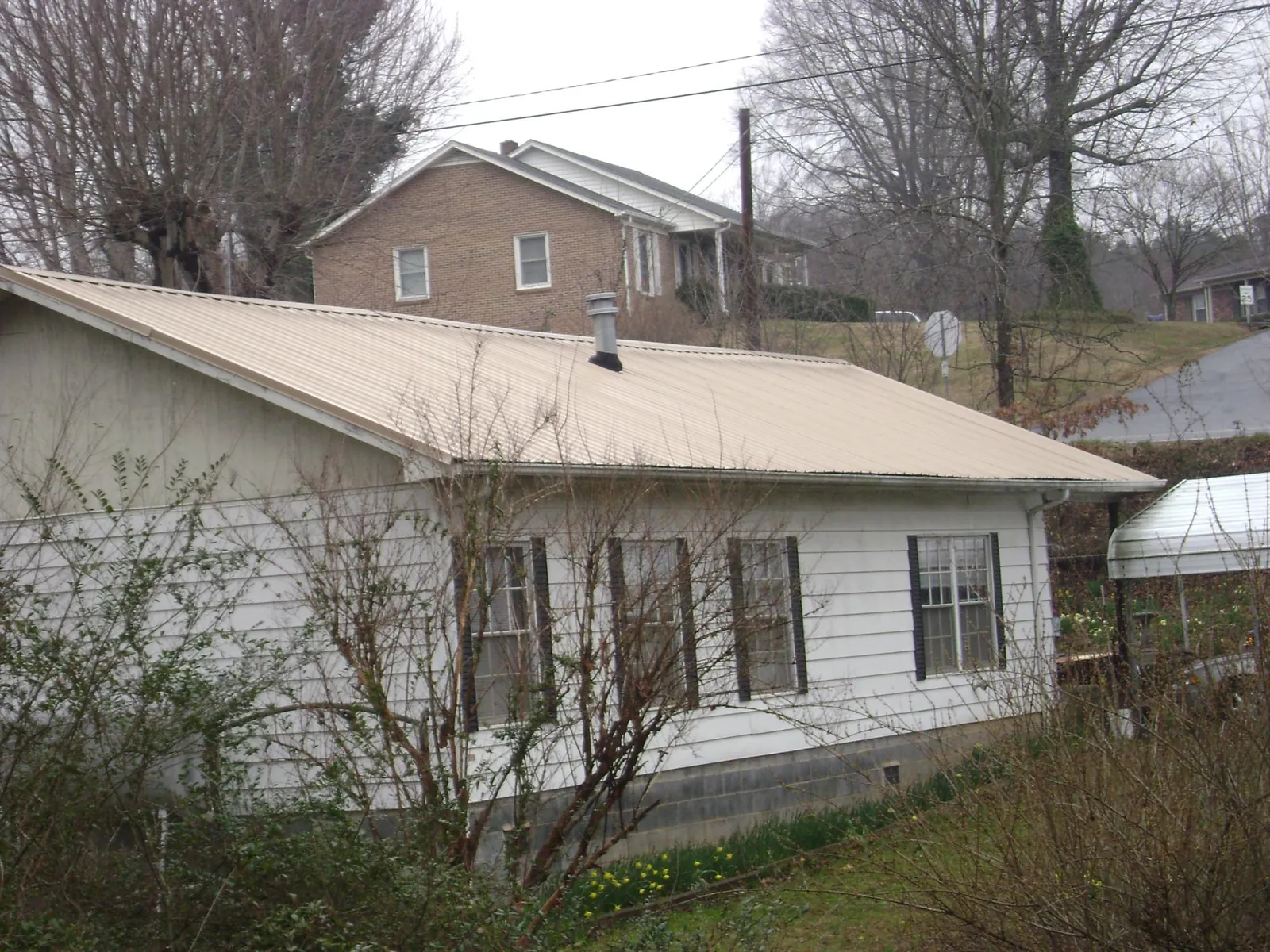 Tan metal roof on a white sided house set into a hillside — Commercial Roofing by Roofing Brothers in South Berwick